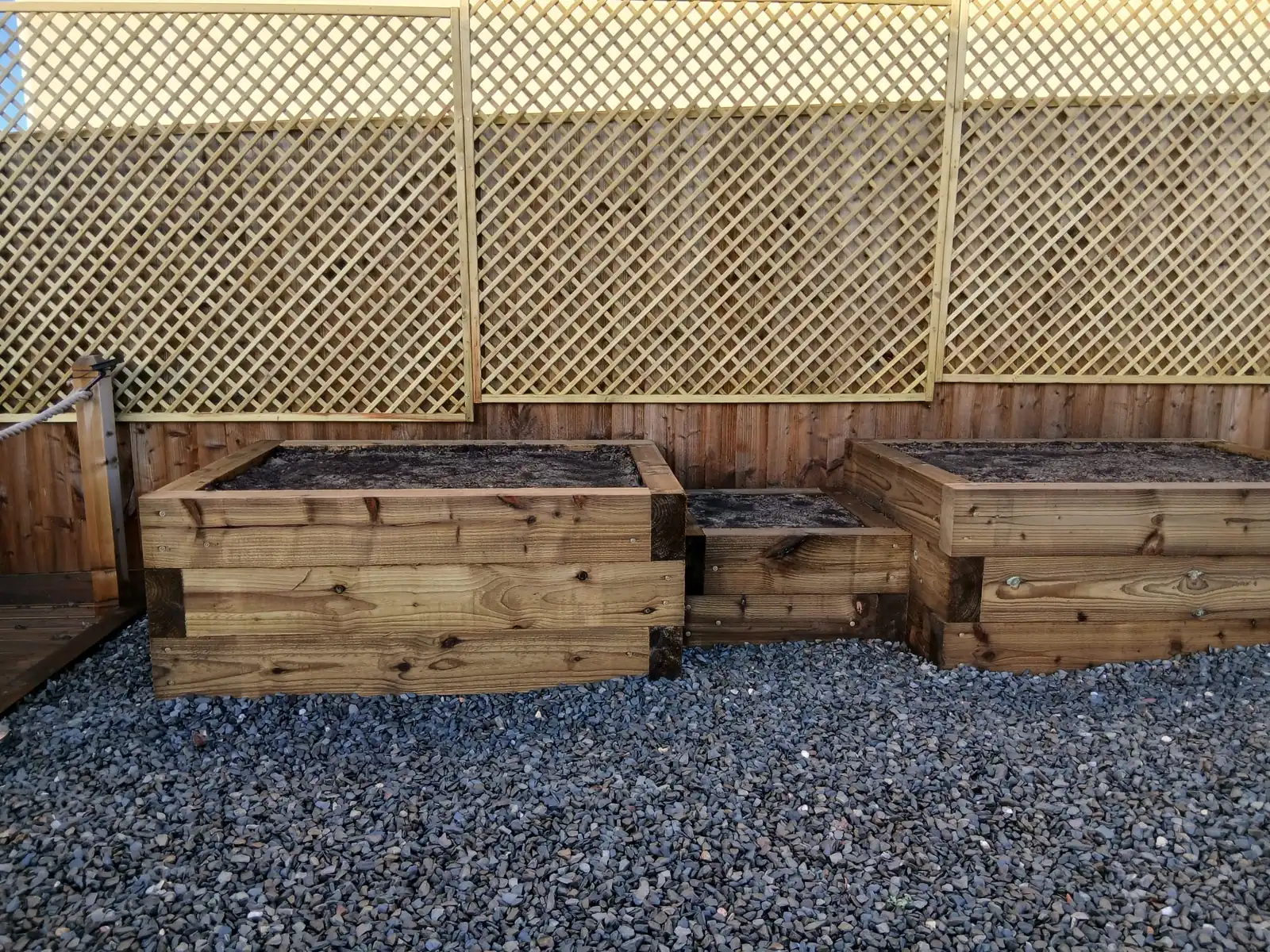 Treated timber sleeper raised planters in blue slate chippings, with diamond lattice trellis on the fence behind
