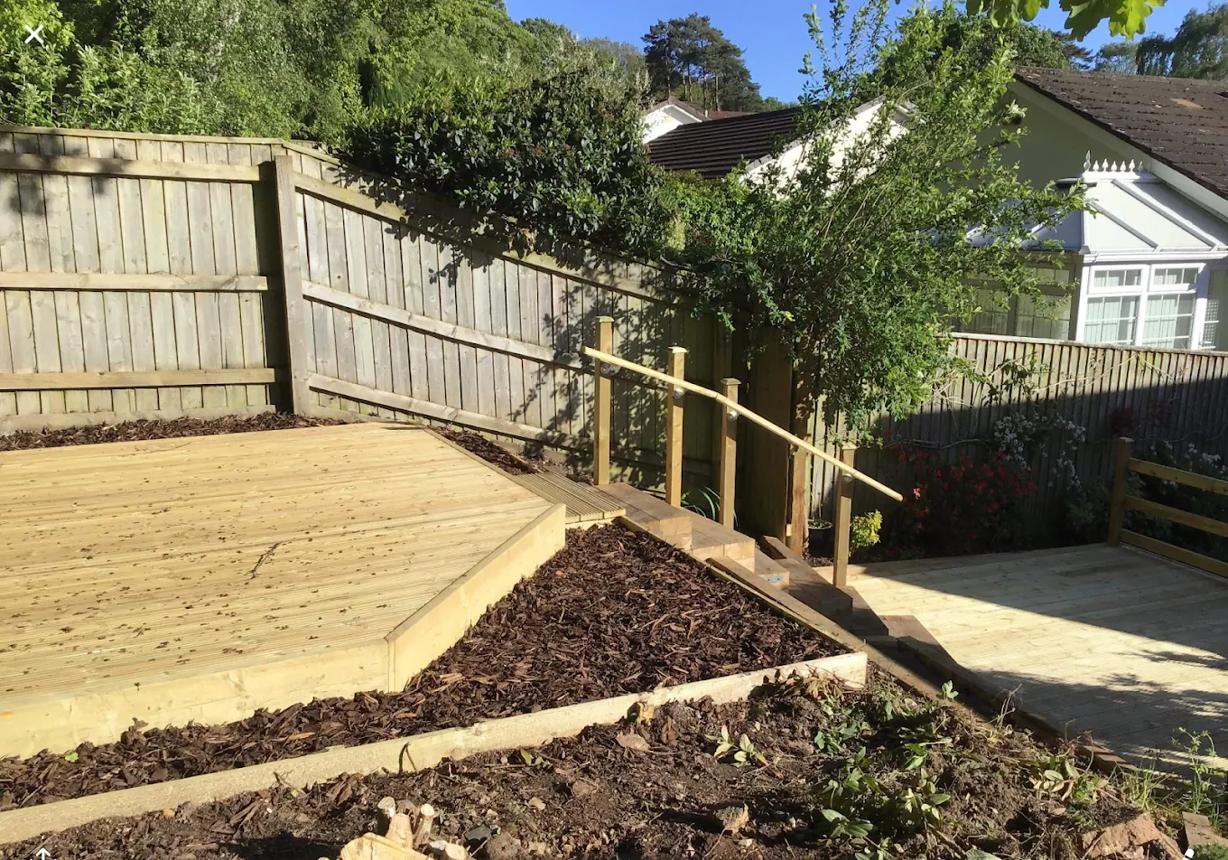 Timber decking with a handrail and steps running down a sloping garden