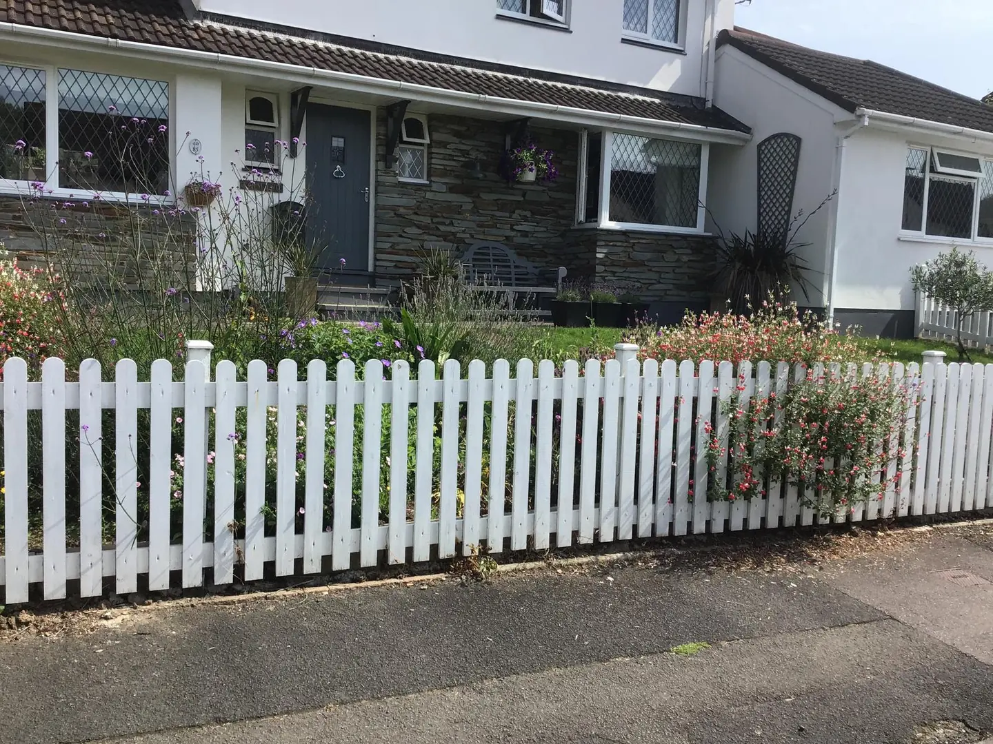 White painted picket fence in front of a planted front garden